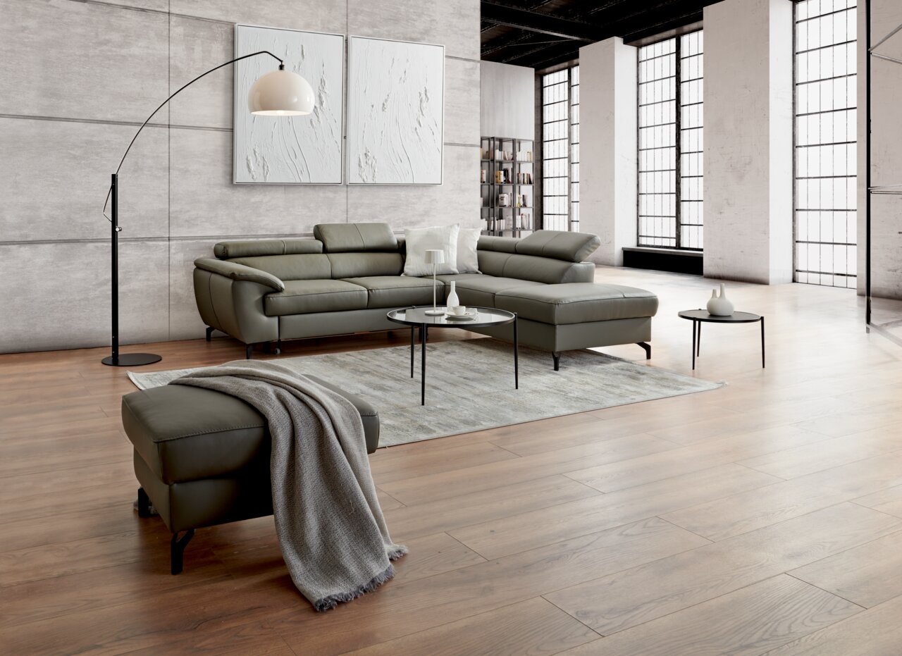 Moderner Wohnraum mit einem Hocker mit Stauraum im Vordergrund, umgeben von einem eleganten Sofa-Set, einem runden Couchtisch und einer Stehlampe, aus der Perspektive des Betrachters auf den Hocker.