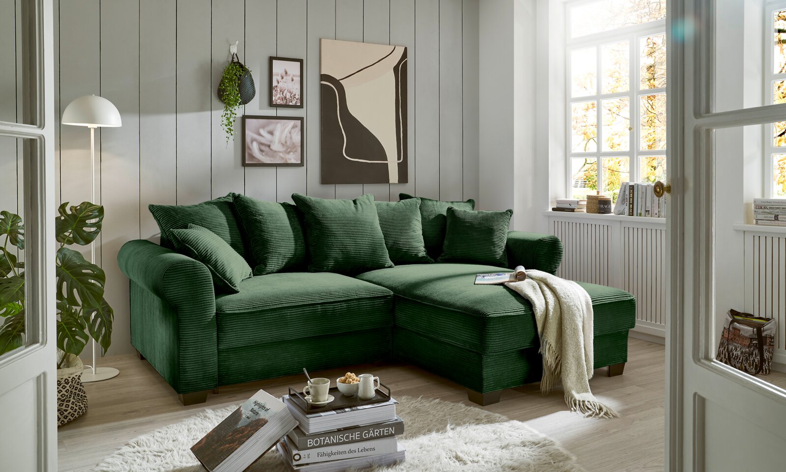 Grünes Ecksofa in einem gemütlichen Wohnzimmer mit moderner Dekoration, von vorne betrachtet.