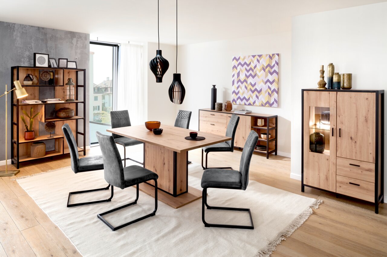 Esszimmer mit modernem Esstisch aus Holz und Metall, umgeben von grauen Stühlen. Im Hintergrund sind ein Regal, ein Sideboard und ein Highboard zu sehen. Perspektive: Frontalansicht des Esstisches.