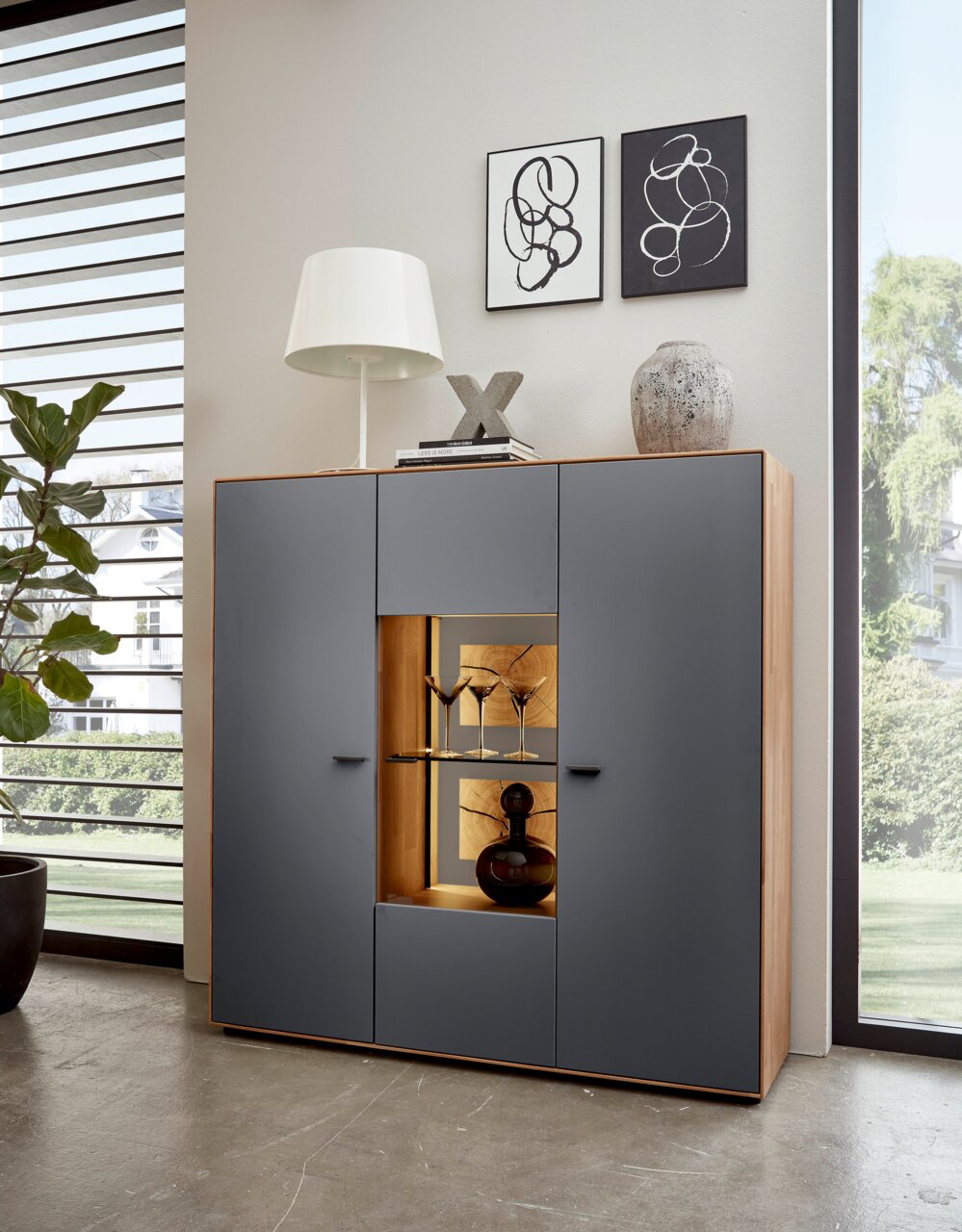 Modernes Highboard mit grauen Türen und Holzrahmen, dekoriert mit einer Lampe und Kunstobjekten, frontal fotografiert.