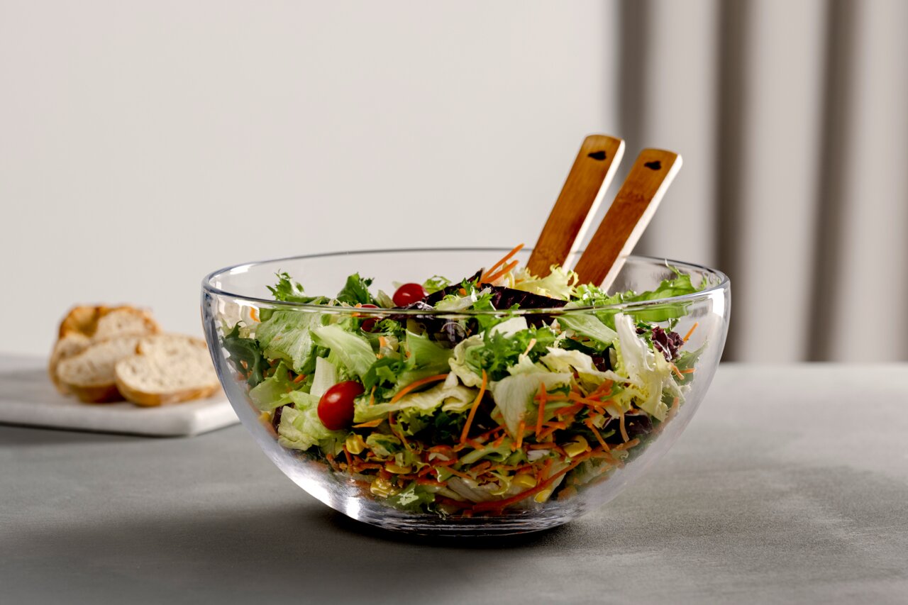 Glasklare Schale mit frischem Salat und Salatbesteck aus Holz, seitliche Perspektive