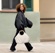 Witte, gewatteerde handtas met ronde handgreep, gedragen door een vrouw terwijl ze loopt, gezien vanaf de zijkant; perspectief: zijaanzicht op heuphoogte in een streetstyle-setting.