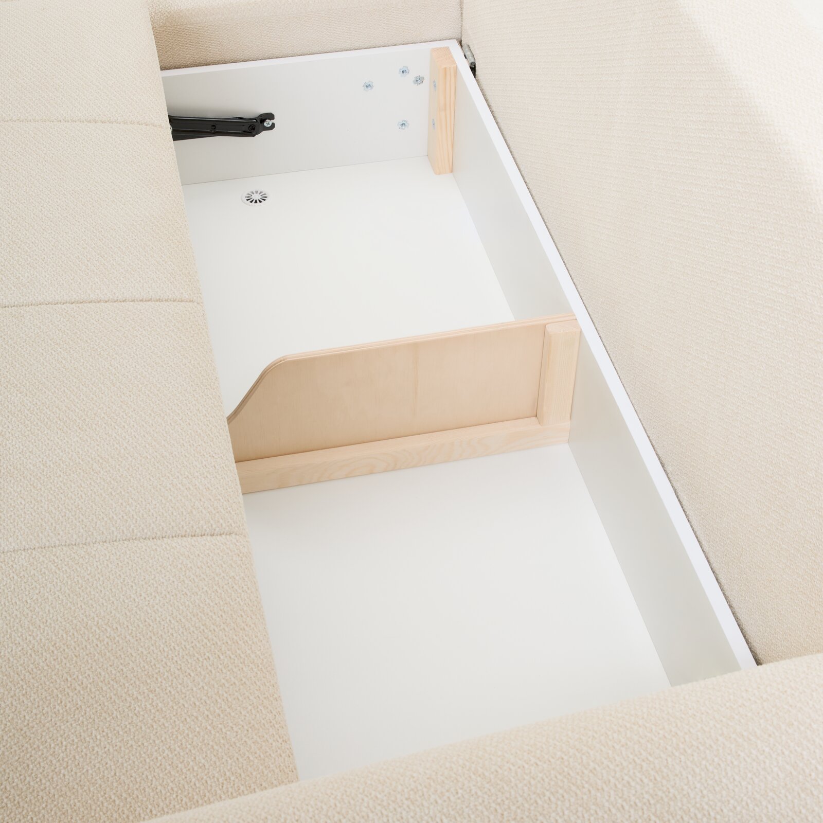 Aufsicht auf den geöffneten Stauraum eines beigen Polsterbetts/Boxspringbetts mit weißem Bettkasten, Holztrennwand und schwarzem Klappbeschlag