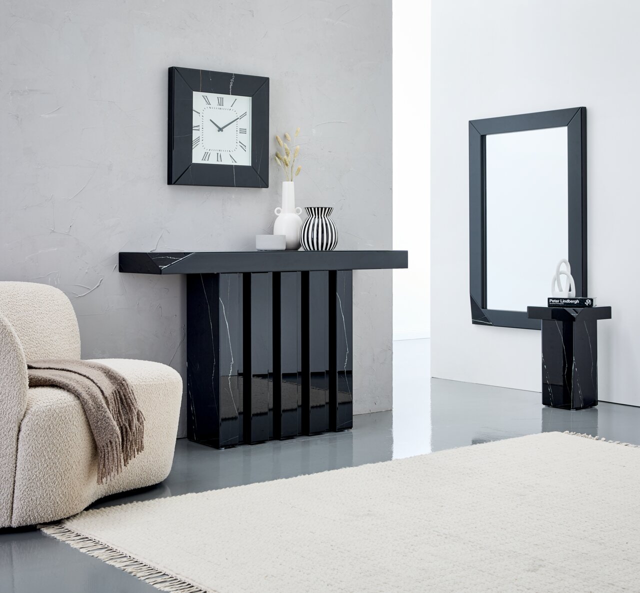 XORA Wanduhr BRONX Moderner Wohnraum mit einem schwarzen Konsolentisch, einem Spiegel, einer Wanduhr und einem Beistelltisch, alle mit Marmoroptik. Perspektive von vorne.