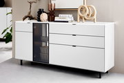Modernes weißes Sideboard mit drei Schubladen und einer Glastür, dekoriert mit Büchern und Skulpturen, seitliche Perspektive.