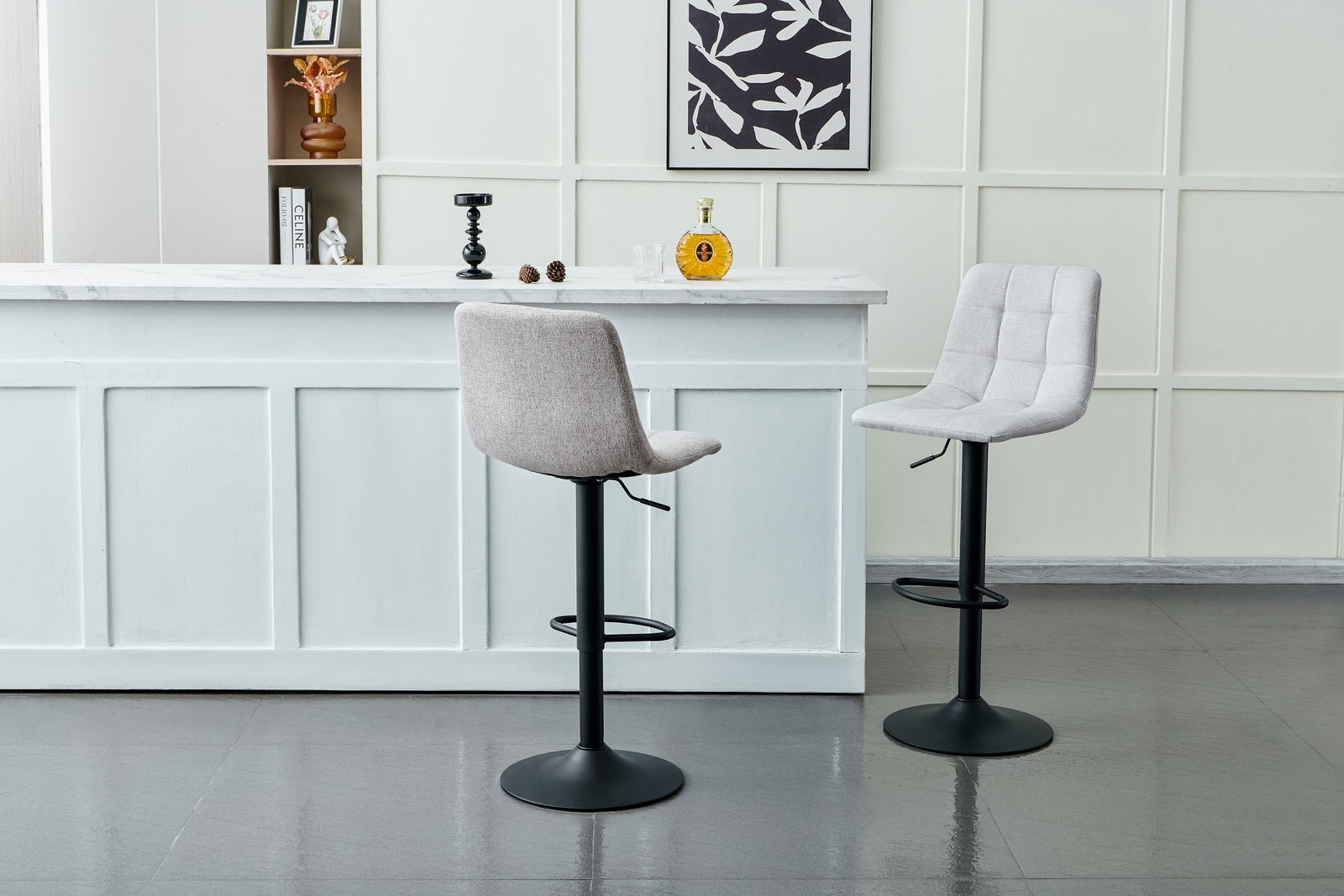 Zwei moderne Barhocker mit schwarzem Fuß und hellgrauer Polsterung, vor einer weißen Theke in einem stilvollen Raum, seitliche Perspektive.