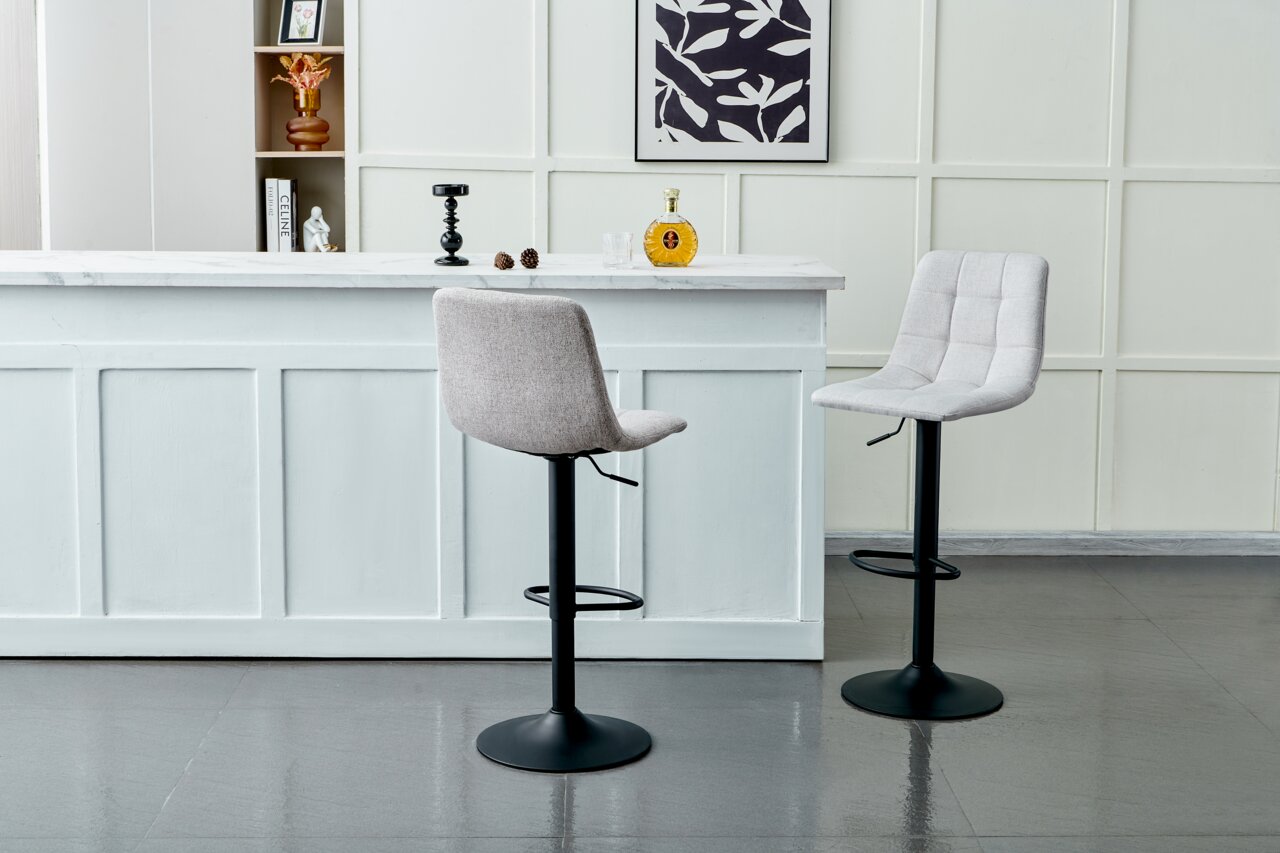 Zwei moderne Barhocker mit schwarzem Fuß und hellgrauer Polsterung, vor einer weißen Theke in einem stilvollen Raum, seitliche Perspektive.