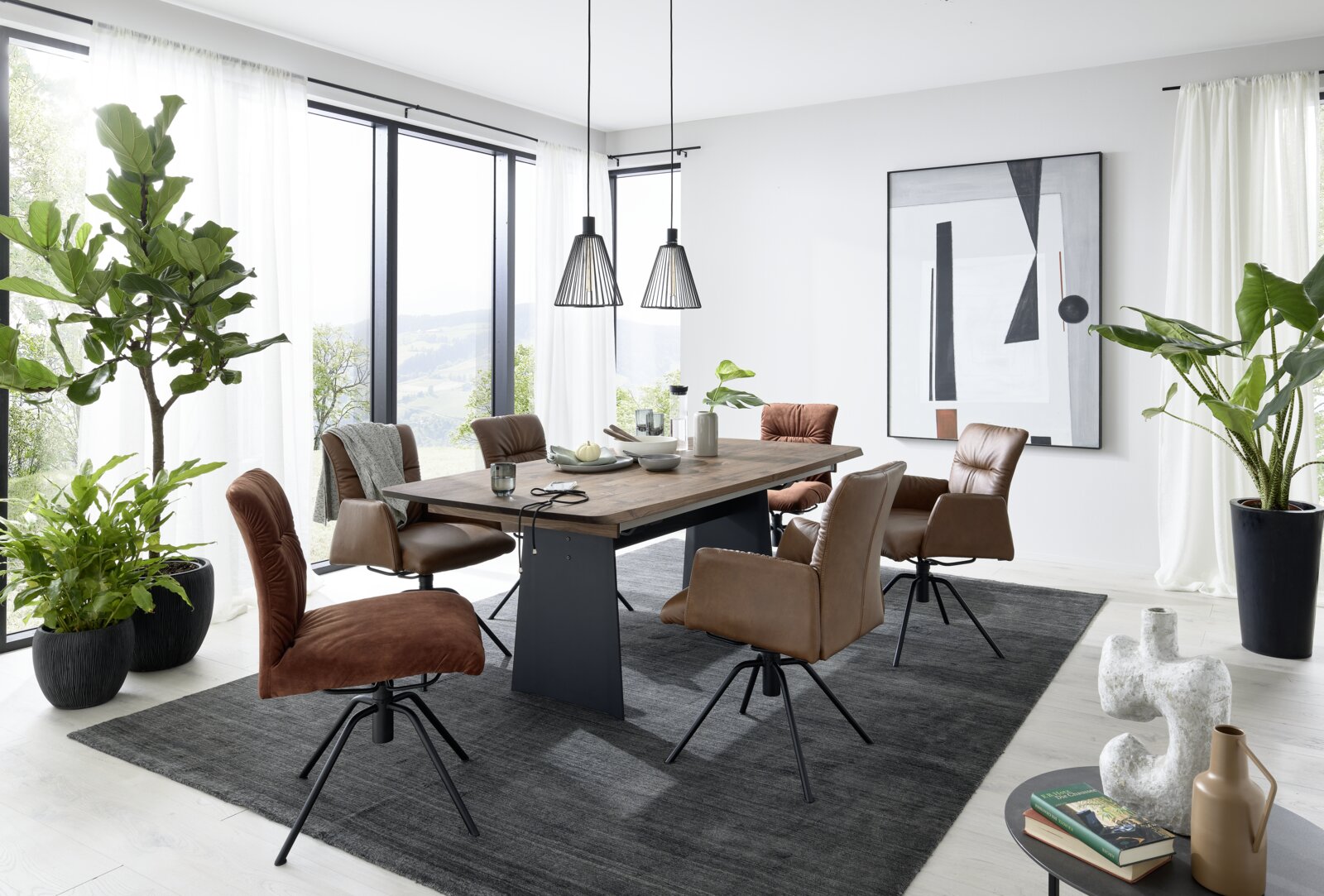 Moderner Essbereich mit einem großen Holztisch und sechs gepolsterten Sesseln in einem hellen Raum mit großen Fenstern, Pflanzen und abstrakter Kunst an der Wand. Perspektive: seitlich.