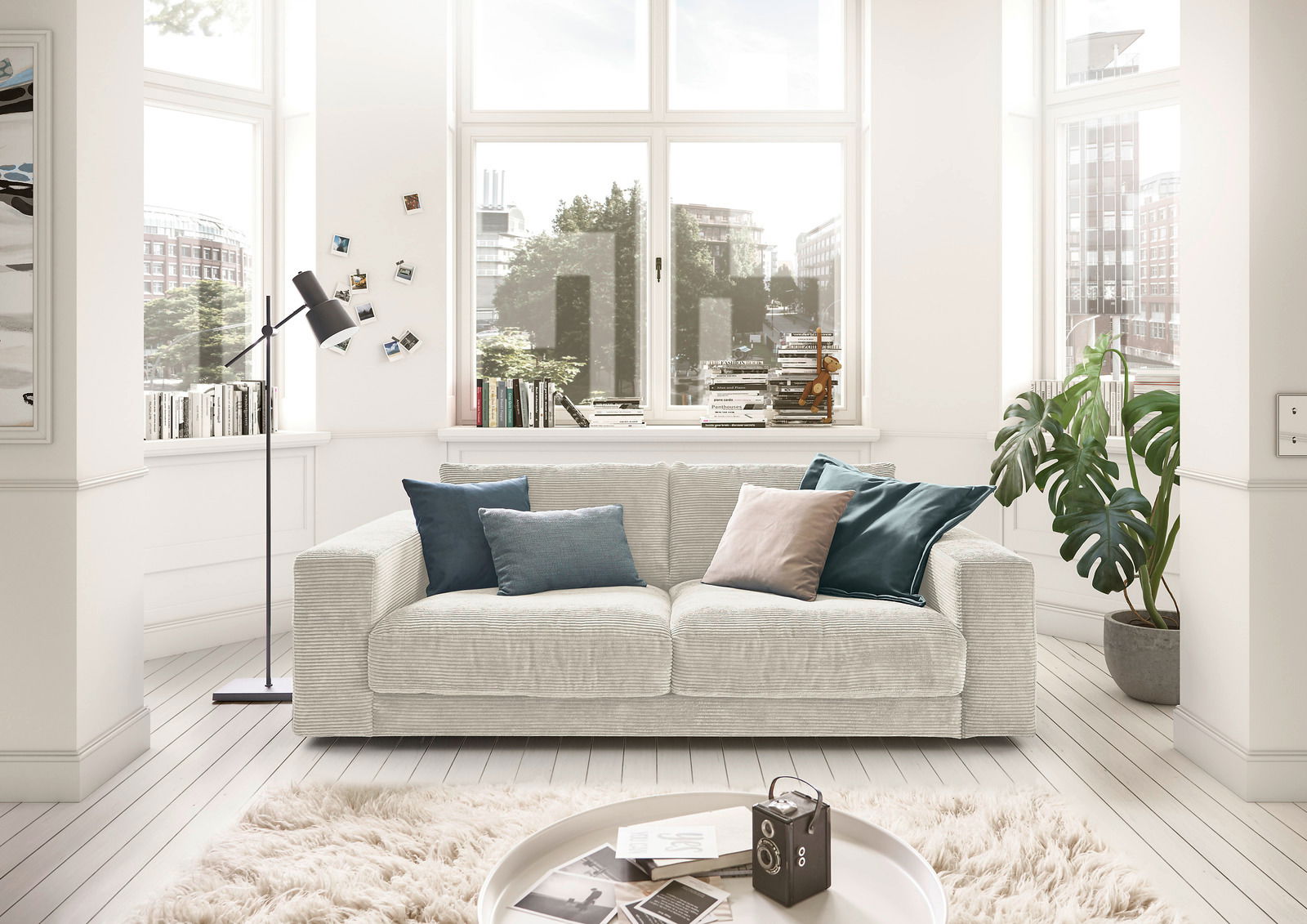 Zweisitzer-Sofa in einem hellen Wohnzimmer mit großen Fenstern, dekoriert mit Kissen in Blau- und Grautönen, aus der Frontalperspektive.