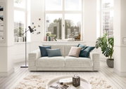 Zweisitzer-Sofa in einem hellen Wohnzimmer mit großen Fenstern, dekoriert mit Kissen in Blau- und Grautönen, aus der Frontalperspektive.