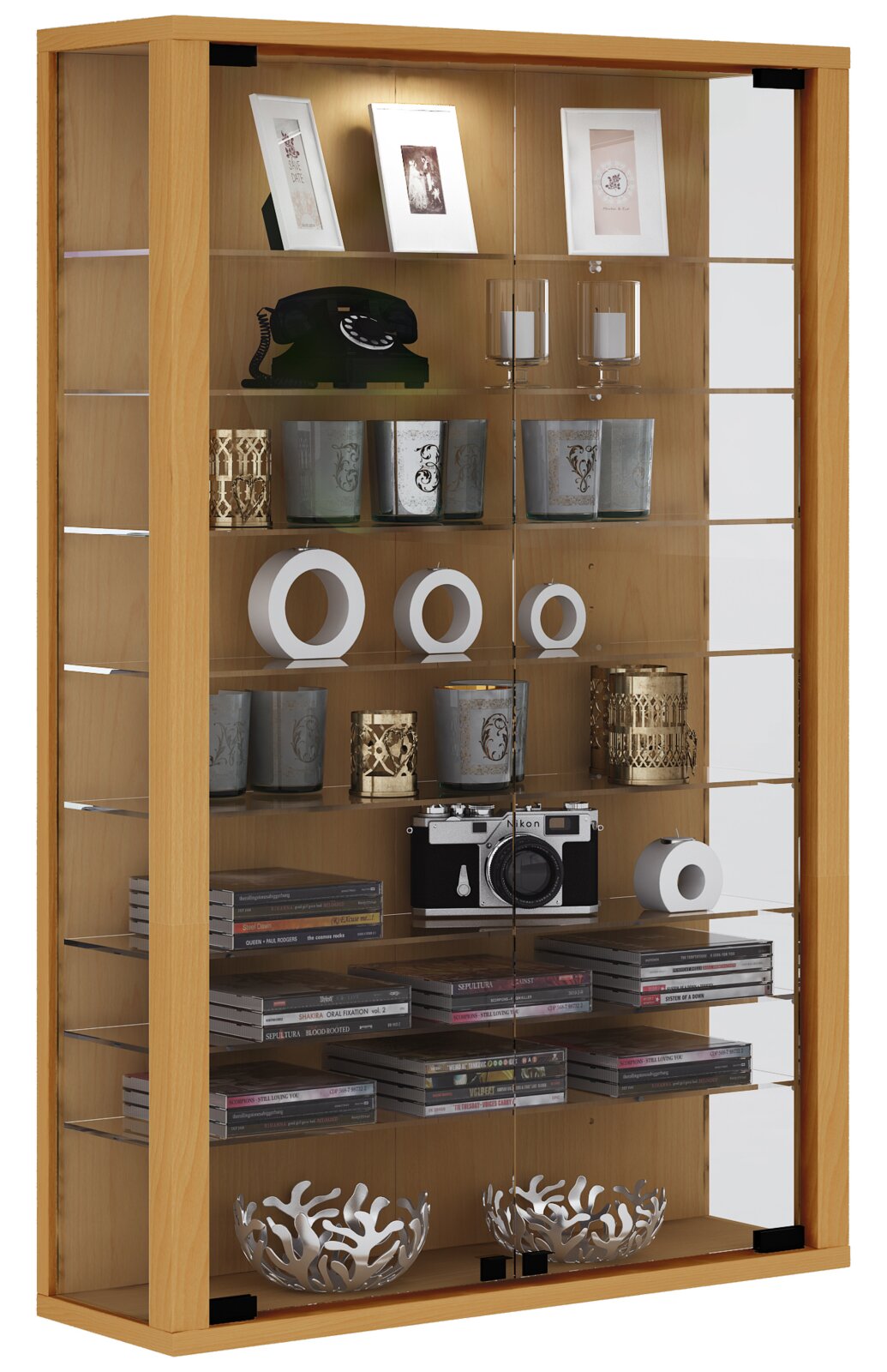 Hohe Vitrine aus hellem Holz mit Glastüren und mehreren Glasböden, dekoriert mit Bilderrahmen, Kerzenhaltern, Telefon, Kamera und CDs, frontal in leichter Perspektive von vorn auf weißem Hintergrund.