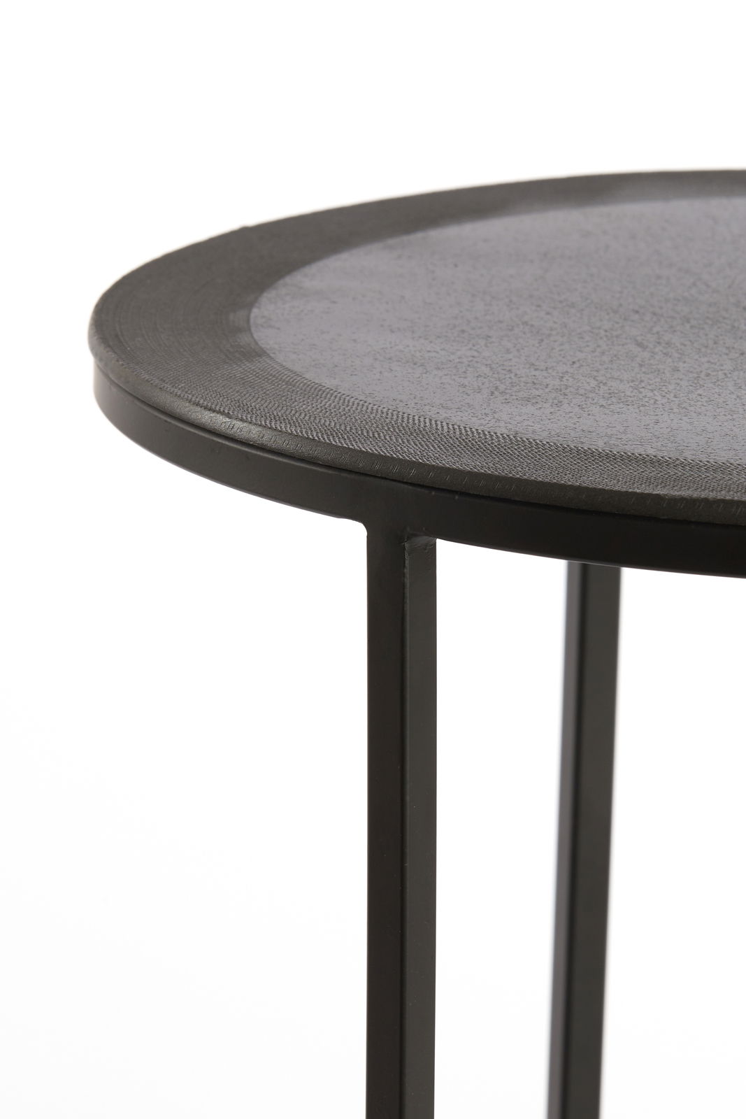 Nahaufnahme eines runden Beistelltisches mit schwarzer Metalloberfläche und schlanken Beinen, seitliche Perspektive.