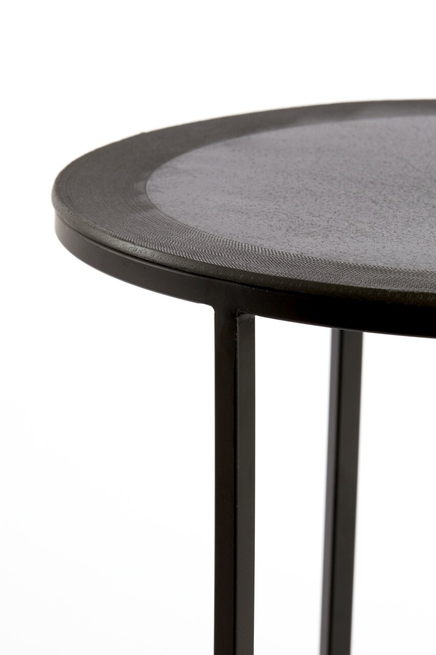 Nahaufnahme eines runden Beistelltisches mit schwarzer Metalloberfläche und schlanken Beinen, seitliche Perspektive.