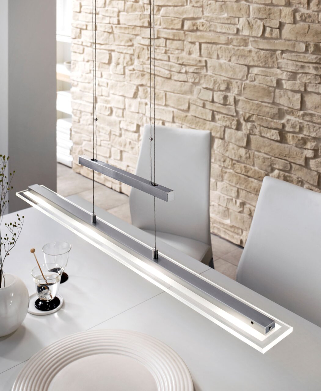 Moderne, längliche LED-Pendelleuchte in Silber mit Seilaufhängung über einem Esstisch, schräg von oben aus der Nähe fotografiert