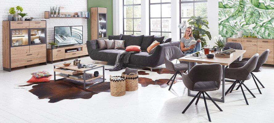 Wohnzimmer mit modernen Möbeln in Holzoptik, bestehend aus einer Vitrine, einem TV-Lowboard, einem Couchtisch und einem Esstisch mit Stühlen. Perspektive: Frontalansicht des gesamten Raumes.