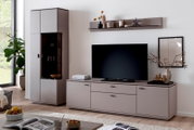 Modernes Wohnzimmer-Setup mit grauem TV-Lowboard und passendem Hochschrank mit Glasvitrine, TV mittig platziert und Wandboard darüber; Frontansicht in leichter Schrägperspektive von links.