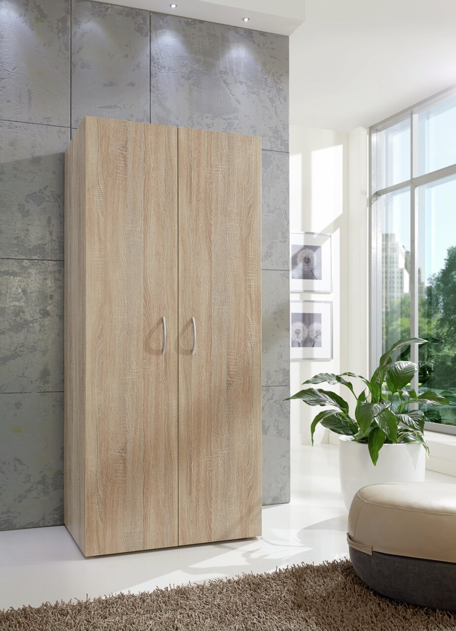 Mehrzweckschrank in Holzoptik, frontal fotografiert, in einem modernen, hellen Raum mit großen Fenstern und Pflanzen.