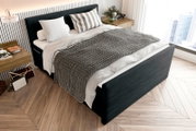 Boxspringbett in modernem Schlafzimmer, seitliche Perspektive, mit grauer Decke und dekorativen Kissen.