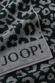 Nahaufnahme eines grauen Duschtuchs mit schwarzem Leopardenmuster und dem Schriftzug 'JOOP!'