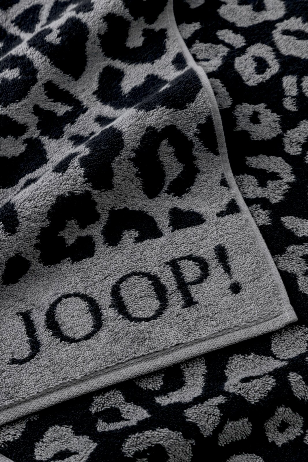 Nahaufnahme eines grauen Duschtuchs mit schwarzem Leopardenmuster und dem Schriftzug 'JOOP!'