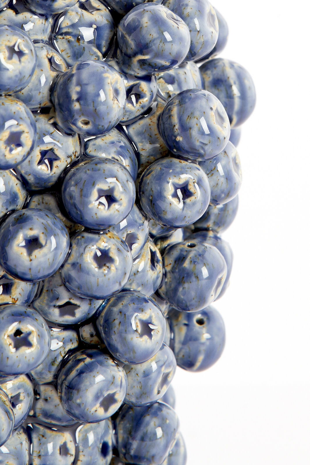 Nahaufnahme einer Vase mit blauen, glänzenden, kugelförmigen Erhebungen, die an Heidelbeeren erinnern. Perspektive von der Seite.