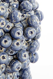 Nahaufnahme einer Vase mit blauen, glänzenden, kugelförmigen Erhebungen, die an Heidelbeeren erinnern. Perspektive von der Seite.
