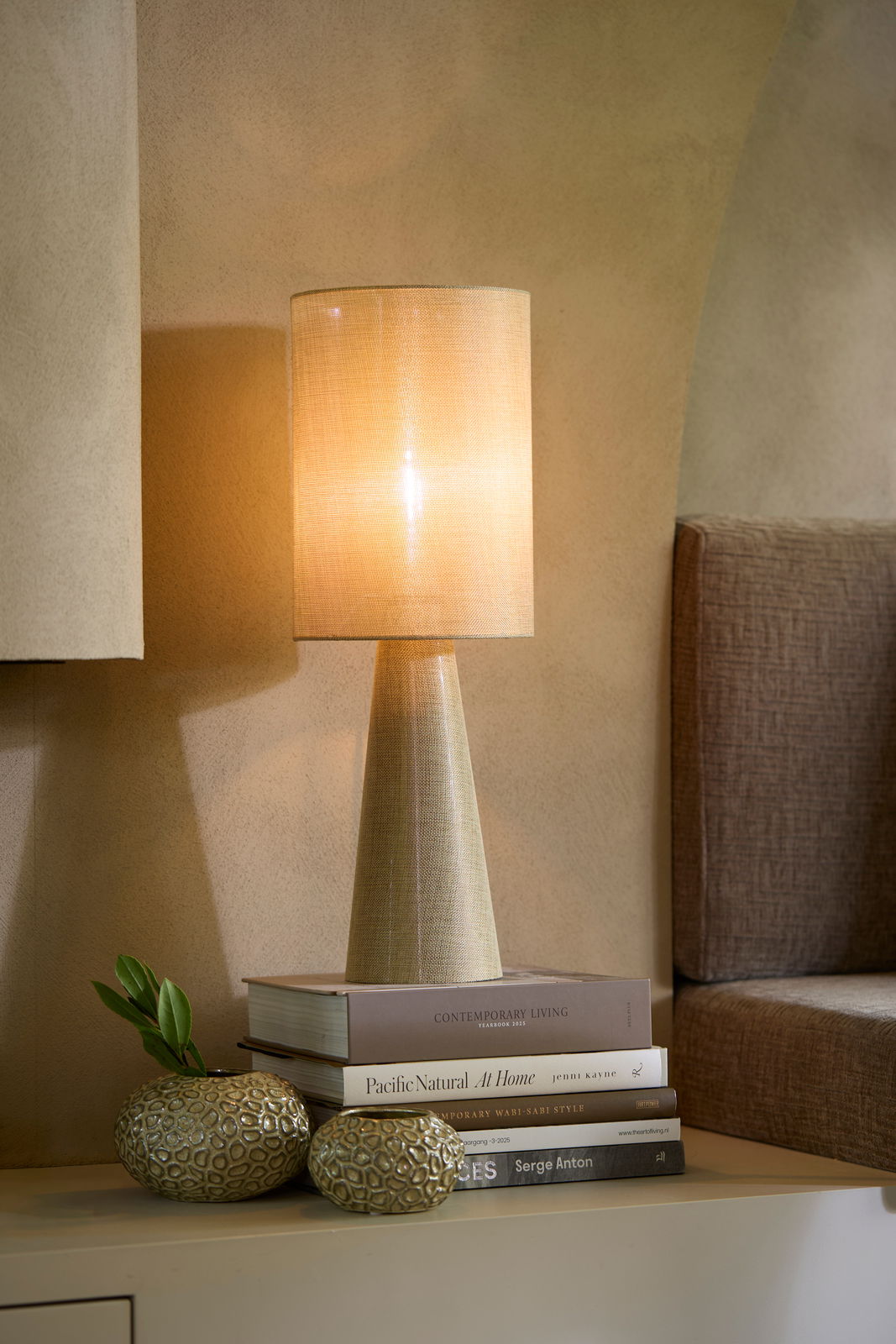 Stimmungsvolle Tischlampe mit konischem Sockel und warmem Licht, seitliche Perspektive auf einem Tisch mit dekorativen Büchern und Vasen.