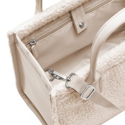 Nahaufnahme einer cremefarbenen Tasche mit weichem, flauschigem Material und robusten Griffen, von oben betrachtet.