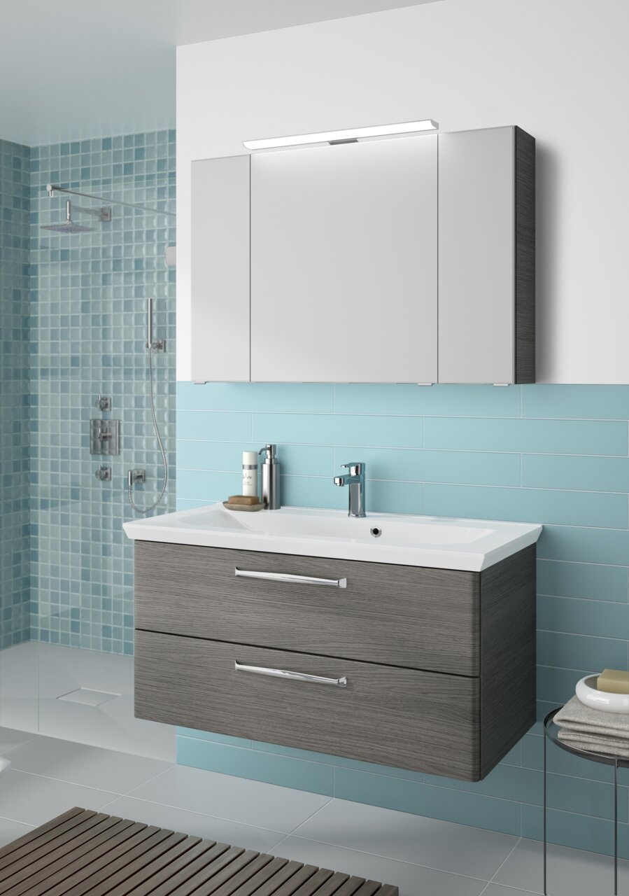 Modern badkamermeubel met grijze lades en een witte wastafel, gezien vanaf de voorkant, in een stijlvolle badkamer met blauwe tegels.