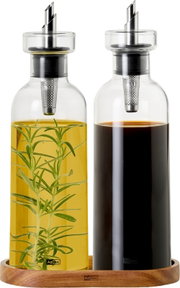 Zwei Glas-Öl- und Essigspender mit Edelstahl-Ausgießer und integriertem Filter auf Holztablett, links gelbes Kräuteröl mit Rosmarinzweig, rechts dunkler Essig; frontale Produktansicht.