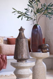 Metallisches Windlicht mit filigranem Muster, auf einem dekorativen Tisch platziert, seitliche Perspektive.