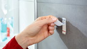 Hand zieht tesa Powerstrip Waterproof von einer grauen Wand ab, seitliche Perspektive