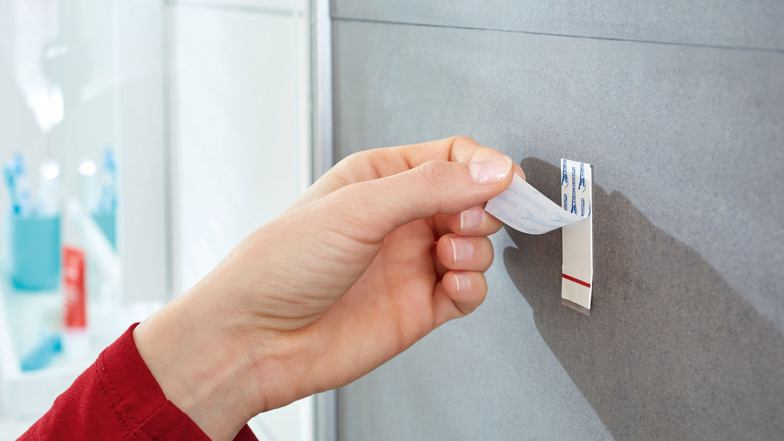 Hand zieht tesa Powerstrip Waterproof von einer grauen Wand ab, seitliche Perspektive