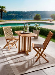 Gartentisch aus Holz mit zwei passenden Stühlen, auf einer Terrasse mit Blick auf einen Pool und einen See, aus der Vogelperspektive fotografiert.