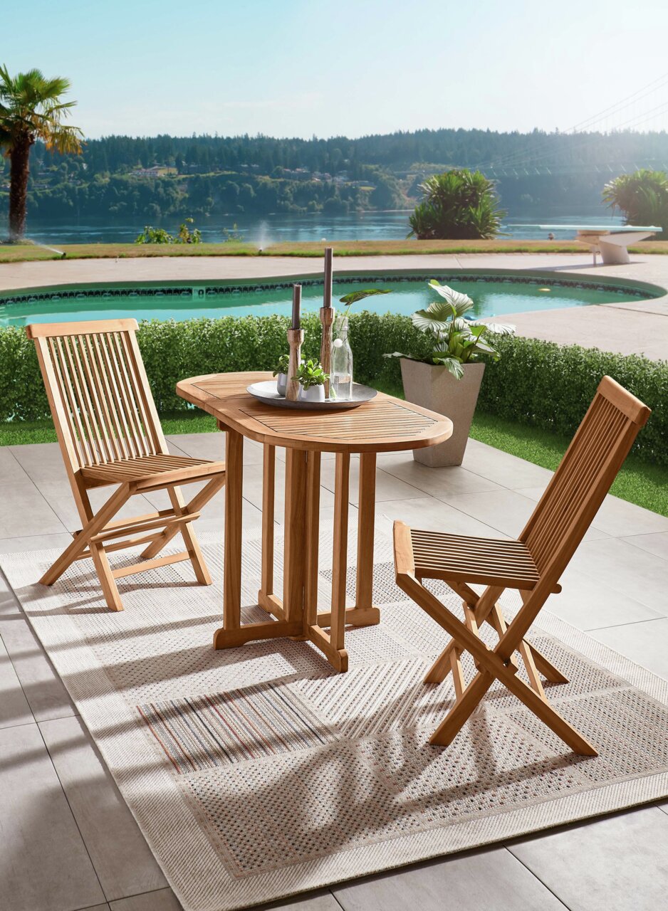Gartentisch aus Holz mit zwei passenden Stühlen, auf einer Terrasse mit Blick auf einen Pool und einen See, aus der Vogelperspektive fotografiert.