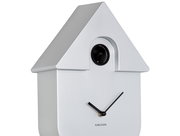 Silberne Wanduhr in Form eines Hauses mit schwarzem Kuckuck und minimalistischen Zeigern, seitliche Perspektive.