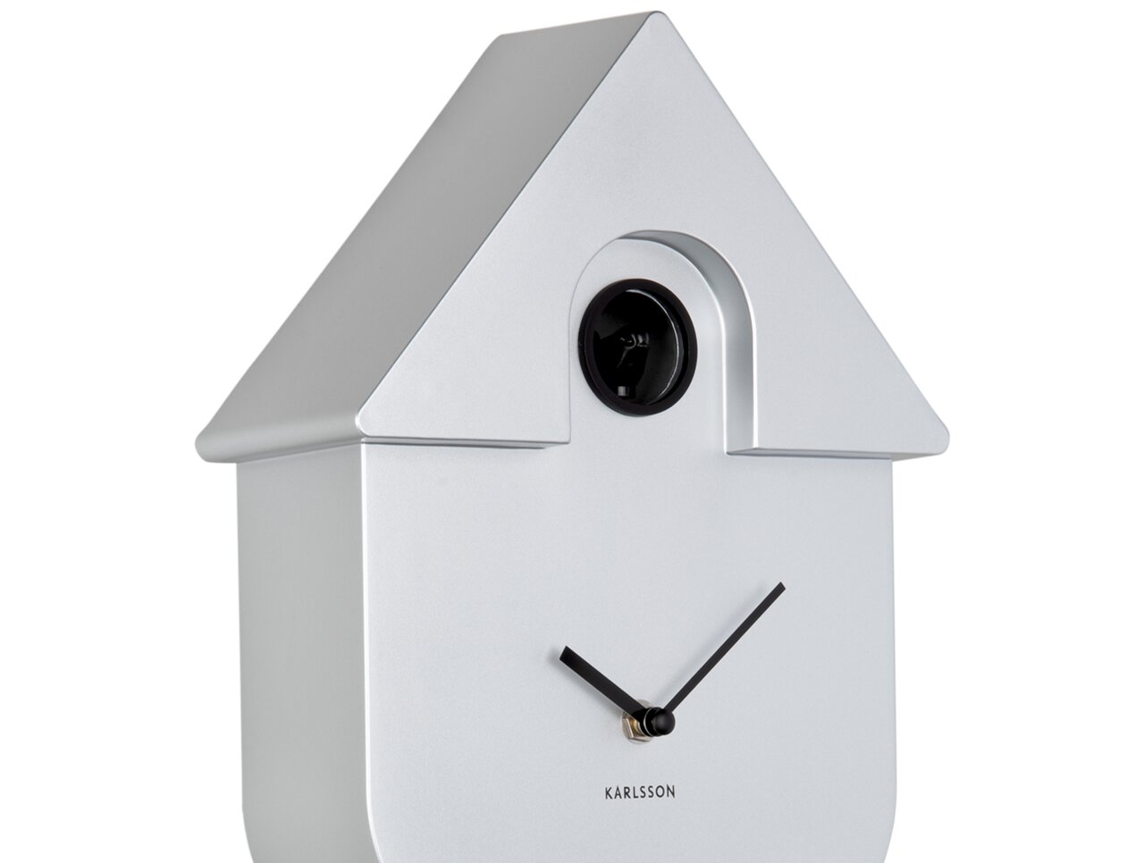 Silberne Wanduhr in Form eines Hauses mit schwarzem Kuckuck und minimalistischen Zeigern, seitliche Perspektive.