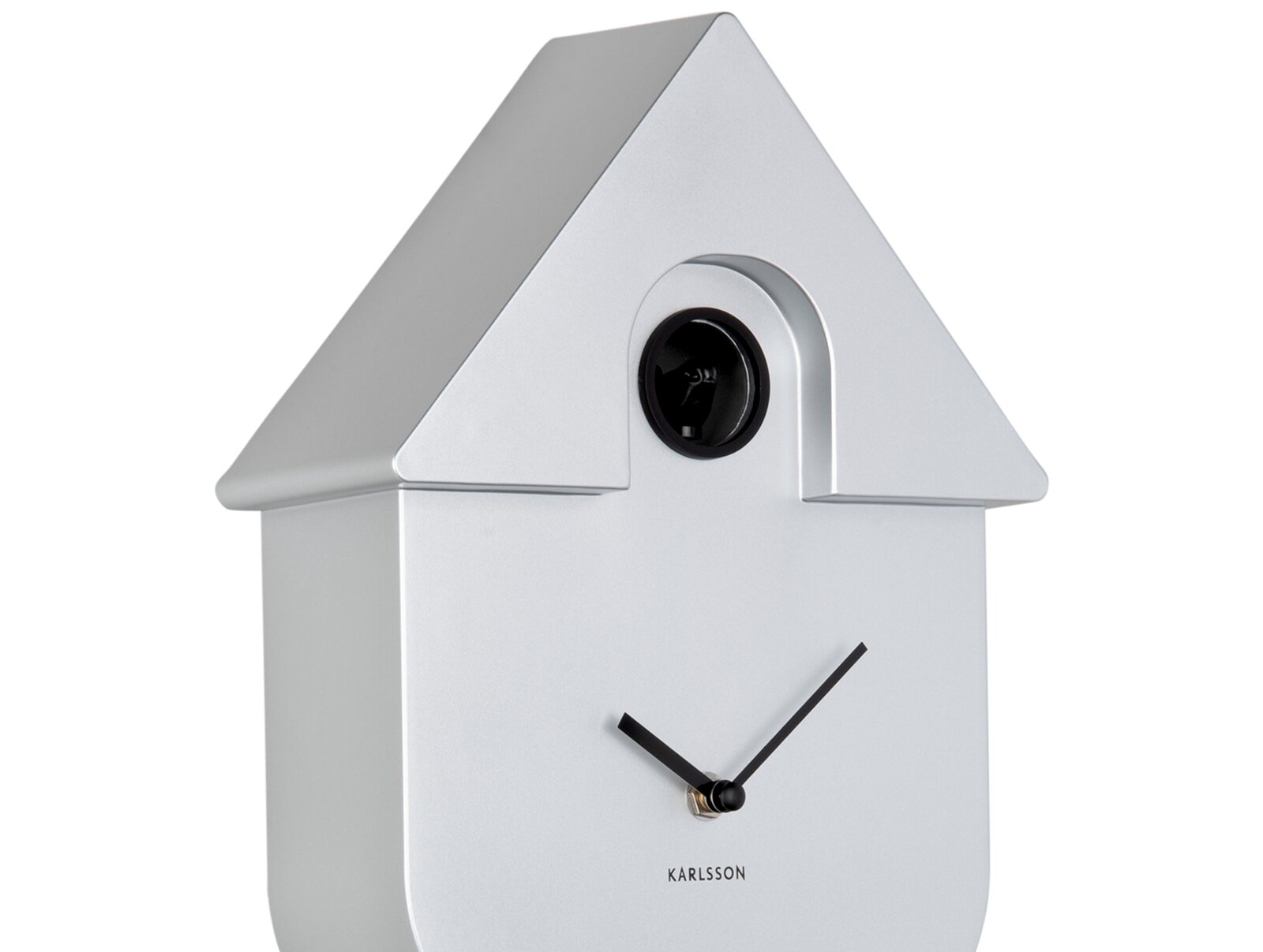 Silberne Wanduhr in Form eines Hauses mit schwarzem Kuckuck und minimalistischen Zeigern, seitliche Perspektive.