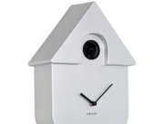 Silberne Wanduhr in Form eines Hauses mit schwarzem Kuckuck und minimalistischen Zeigern, seitliche Perspektive.