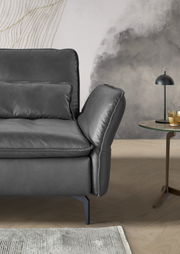 Detailansicht eines modernen, dunkelgrauen Longchairs mit eleganten Metallfüßen, im Vordergrund ein Beistelltisch mit Lampe und Glas. Perspektive von der Seite.