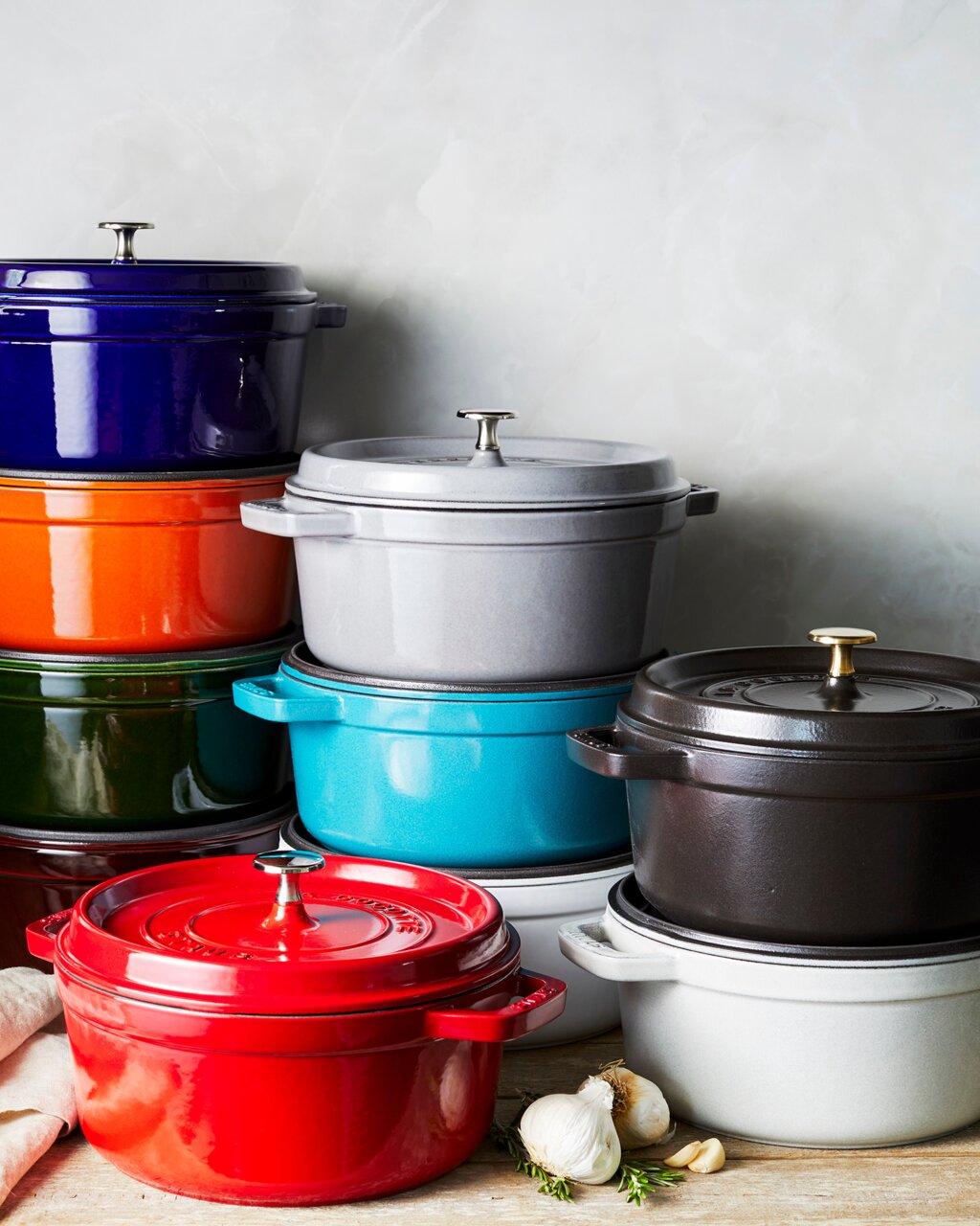 Verschiedene bunte Bräter Cocotte 24cm rund, gestapelt in einer seitlichen Perspektive.