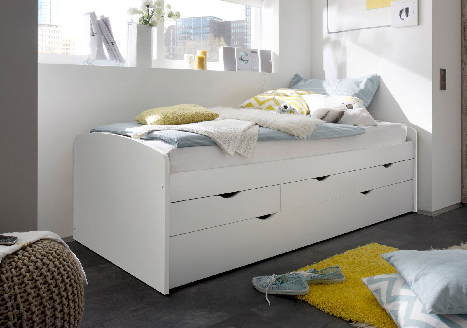 Weiße Tandemliege mit mehreren Schubladen, dekoriert mit Kissen und Decken, seitliche Perspektive