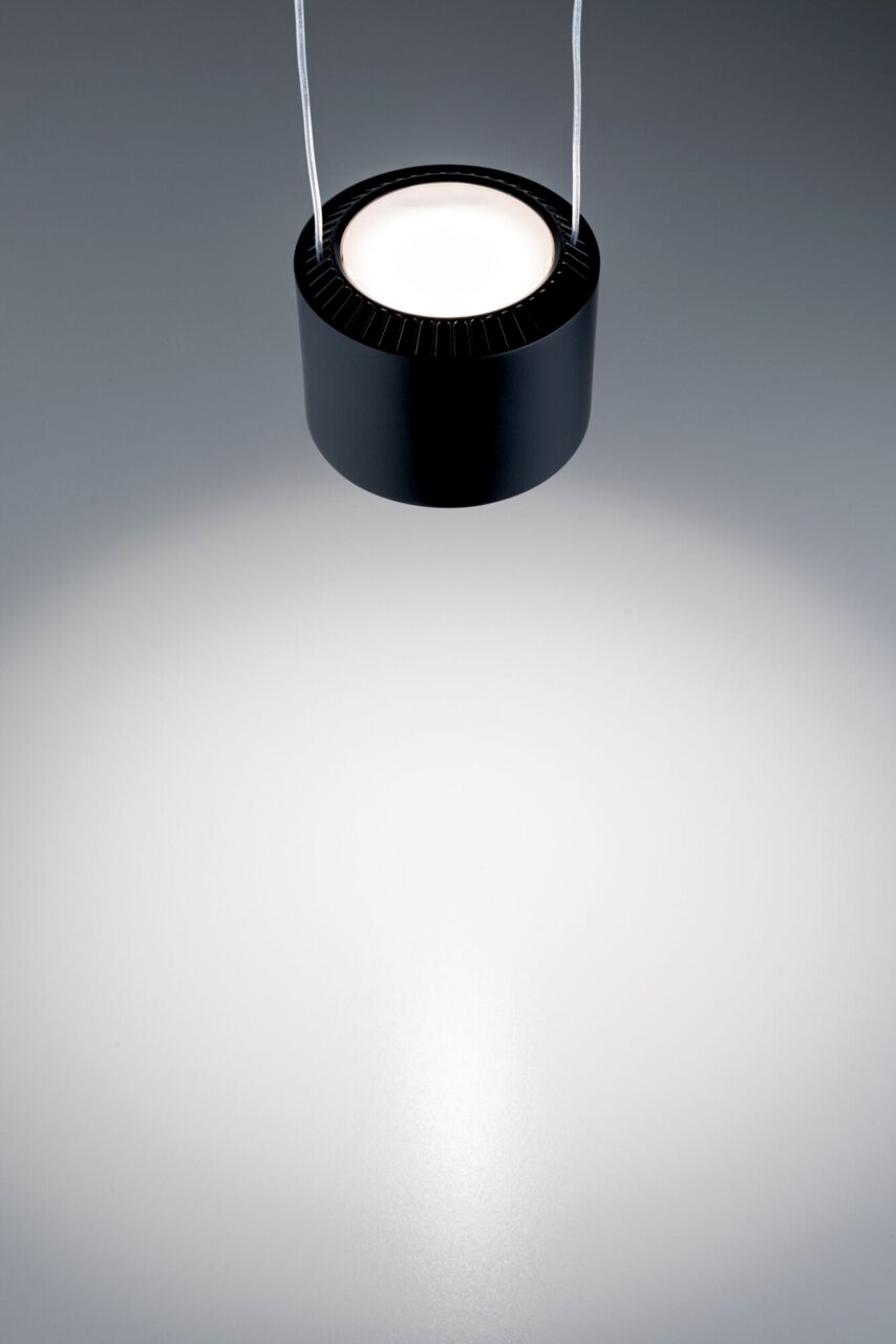 Schwarzes, zylindrisches Pendelleuchte von oben betrachtet, mit hellem Lichtstrahl auf grauem Hintergrund.