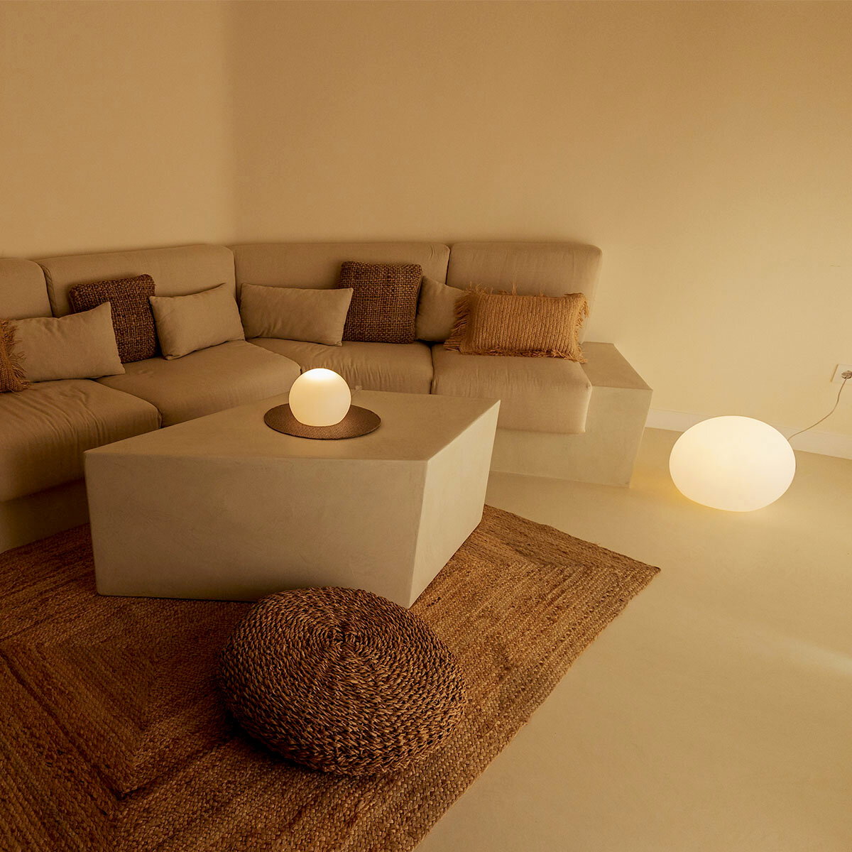 Gemütliches Wohnzimmer mit beigem Ecksofa, quadratischem Couchtisch und leuchtenden Kugellampen auf Tisch und Boden, aufgenommen aus leicht erhöhter Frontperspektive.