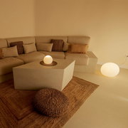 Gemütliches Wohnzimmer mit beigem Ecksofa, quadratischem Couchtisch und leuchtenden Kugellampen auf Tisch und Boden, aufgenommen aus leicht erhöhter Frontperspektive.