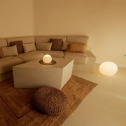 Gemütliches Wohnzimmer mit beigem Ecksofa, quadratischem Couchtisch und leuchtenden Kugellampen auf Tisch und Boden, aufgenommen aus leicht erhöhter Frontperspektive.