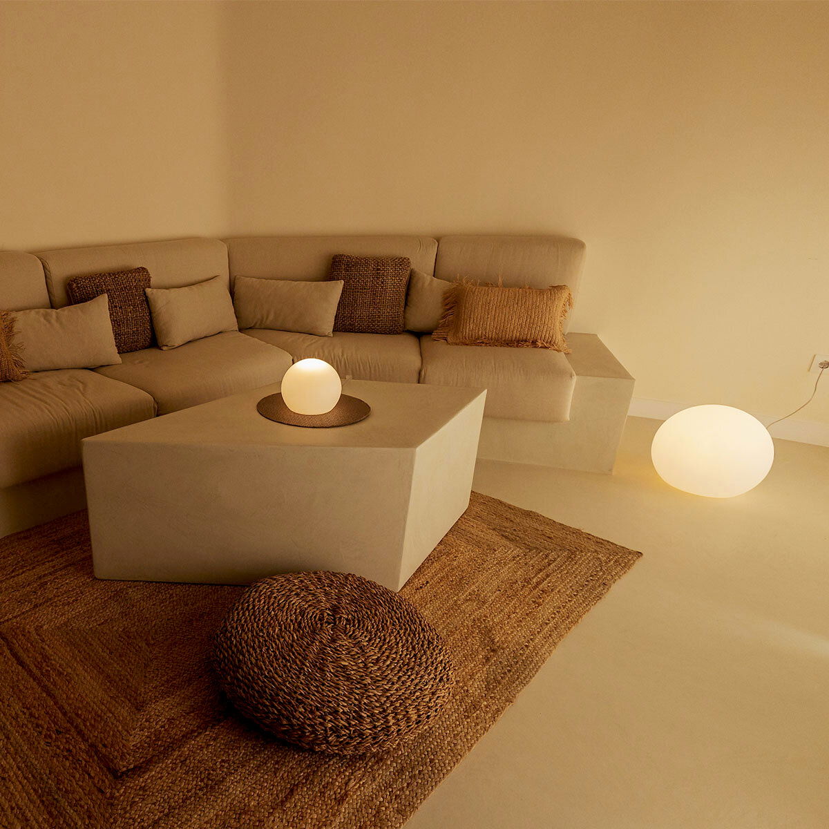 Gemütliches Wohnzimmer mit beigem Ecksofa, quadratischem Couchtisch und leuchtenden Kugellampen auf Tisch und Boden, aufgenommen aus leicht erhöhter Frontperspektive.