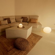 Gezellige woonkamer met een beige hoekbank, een vierkante salontafel en heldere bolvormige lampen op de tafel en op de vloer, gefotografeerd vanuit een iets verhoogd vooraanzicht.