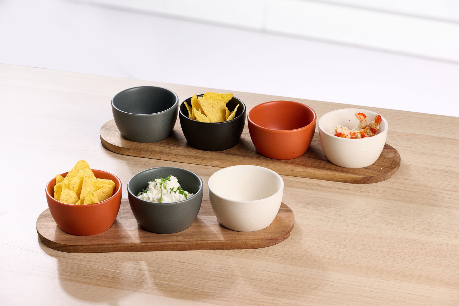 Dipschalen-Set aus fünf Schalen in verschiedenen Farben auf zwei Holztabletts, gefüllt mit Snacks und Dips, aus der Vogelperspektive fotografiert.