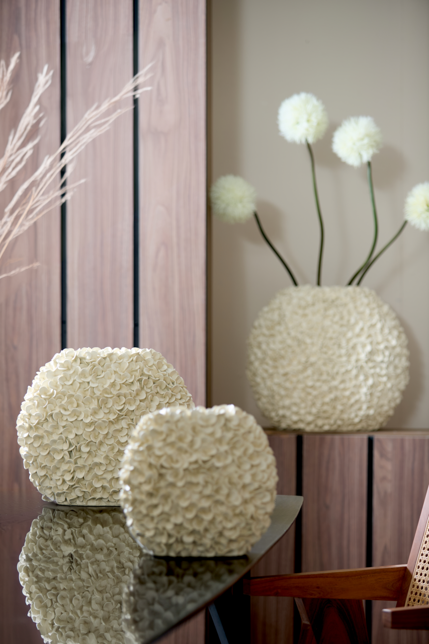 Light&Living Vase PHYLIA Zwei cremefarbene Vasen mit blütenartiger Struktur auf einem Tisch, im Hintergrund eine größere Vase mit dekorativen Blumen, seitliche Perspektive.